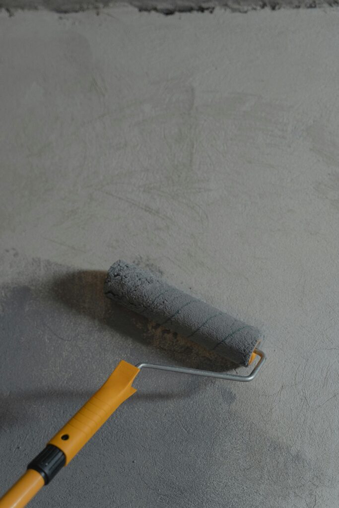 pexels-photo-6474490-6474490 Close-up of a paint roller applying gray paint on a wall, ideal for renovation themes.